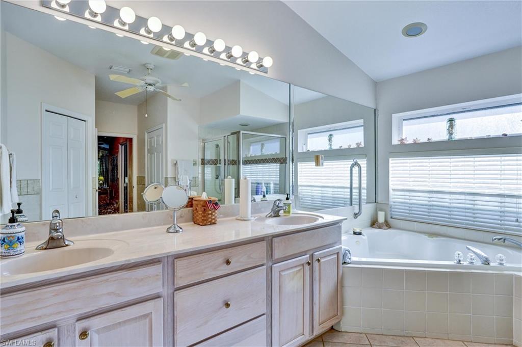 Spacious bathroom featuring a double vanity with light-toned cabinetry and integrated sinks, an expansive mirror with strip lighting, a built-in corner soaking tub, and a separate glass-enclosed shower