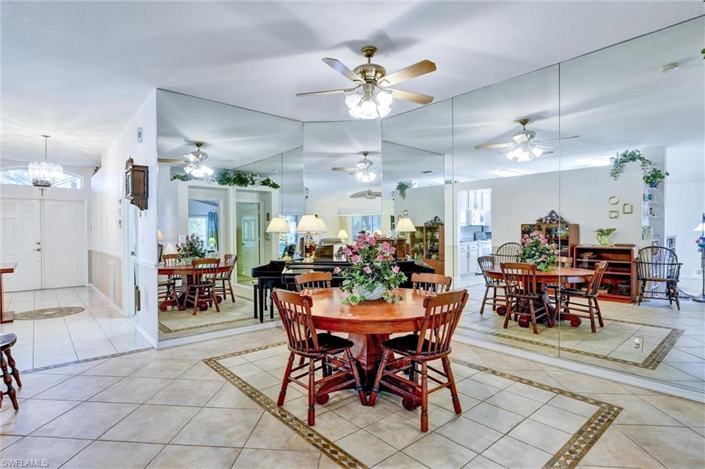 Spacious dining area featuring a prominent mirrored wall, ceiling fan with light fixture, and tile flooring with decorative inlay