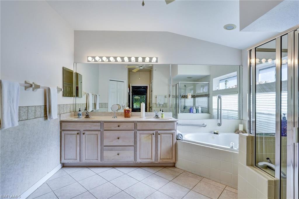 Dual vanity with integrated sinks, large mirrored wall, tile flooring, built-in bathtub, and separate glass-enclosed shower