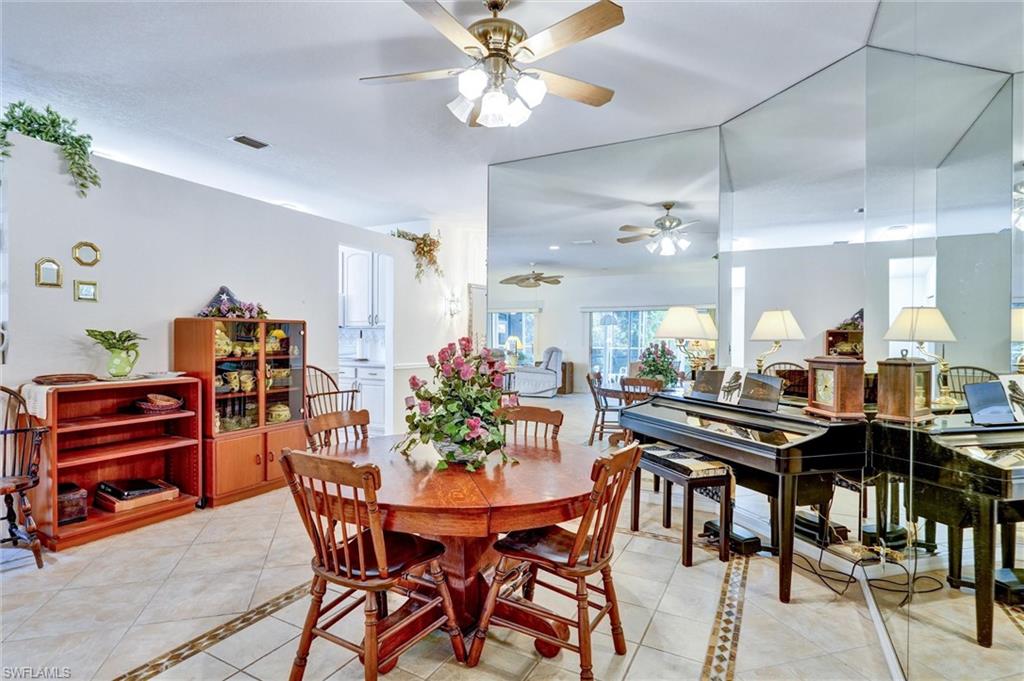 Dining area featuring a ceiling fan with integrated lighting, mirrored wall accents, tile flooring with decorative inlay, and a built-in display cabinet