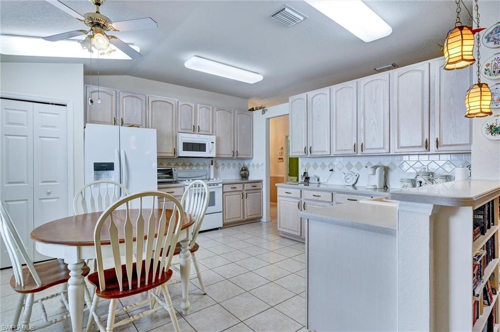 Kitchen featuring white cabinetry, tile flooring, white appliances, and a built-in breakfast bar