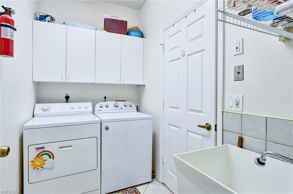 Dedicated laundry area featuring white wall cabinetry, a utility sink, and tiled flooring