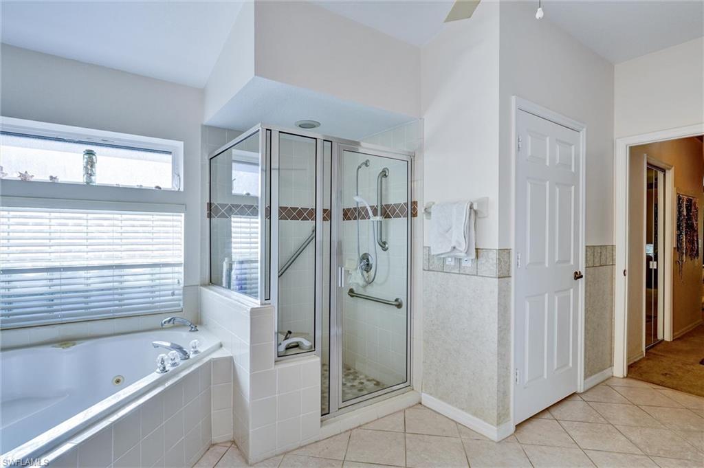 Spacious bathroom featuring a built-in jetted tub, a glass-enclosed shower with decorative tile accents, and tiled flooring