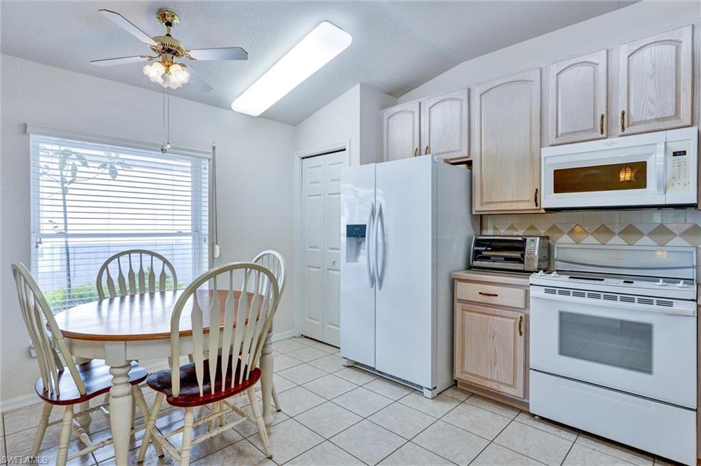 Kitchen featuring tile flooring, vaulted ceiling, ceiling fan with light fixture, built-in microwave, and a window with horizontal blinds