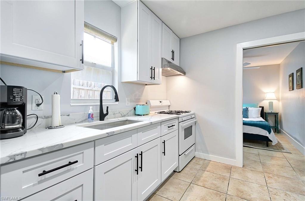 Kitchen with white gas range, light stone countertops, white cabinets, under cabinet range hood, and light tile patterned flooring