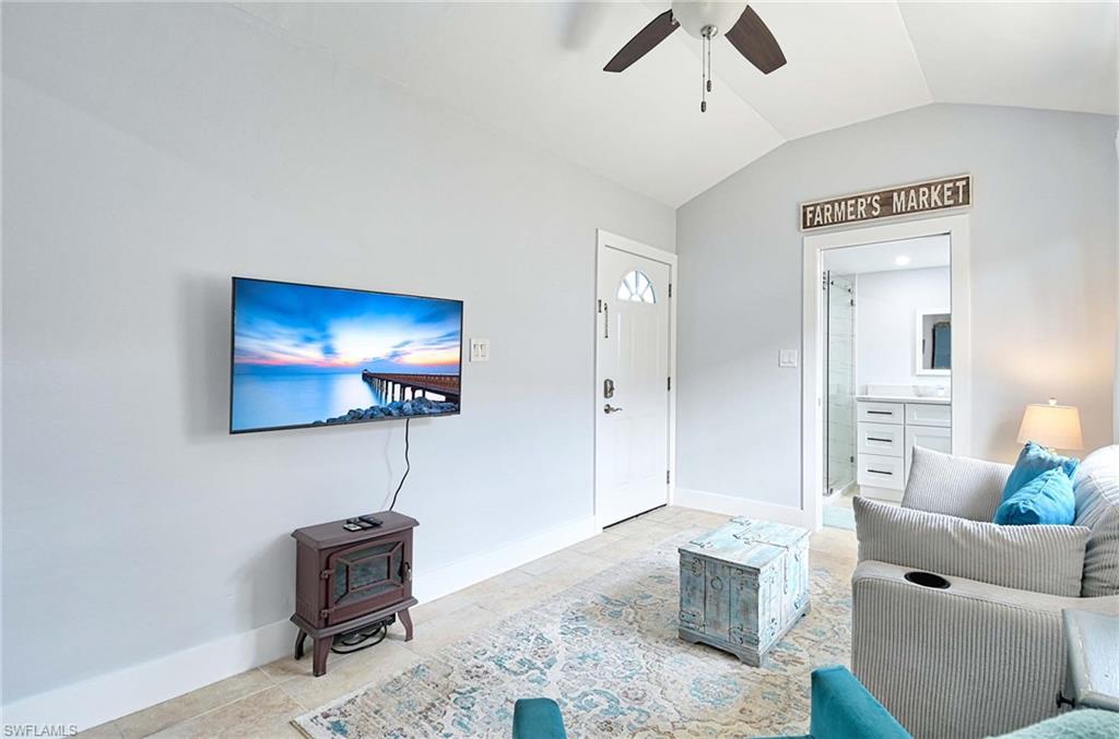 Living area featuring a ceiling fan, a wood stove, and lofted ceiling