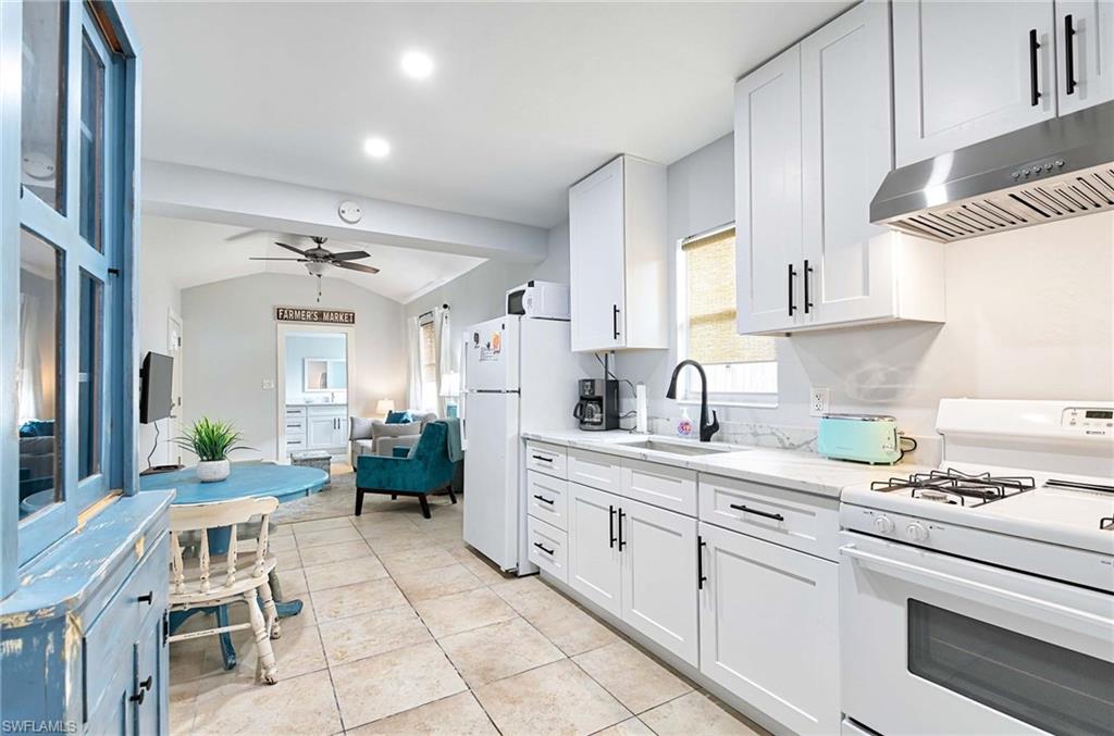 Kitchen featuring white appliances, white cabinetry, ceiling fan, under cabinet range hood, and light tile patterned floors
