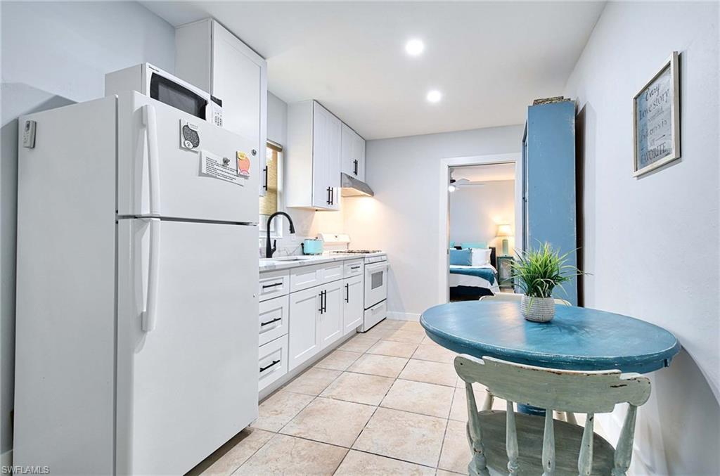 Kitchen with white appliances, white cabinetry, light tile patterned floors, recessed lighting, and under cabinet range hood