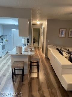 Kitchen with white cabinetry, a breakfast bar, a textured ceiling, dark wood-type flooring, and white range with electric cooktop