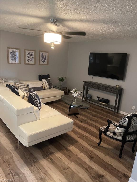 Living area featuring a textured ceiling, dark wood-style floors, and ceiling fan