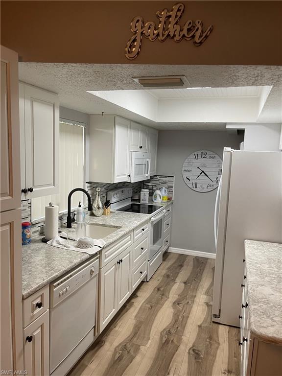 Kitchen featuring white appliances, backsplash, white cabinets, light wood-style flooring, and a tray ceiling