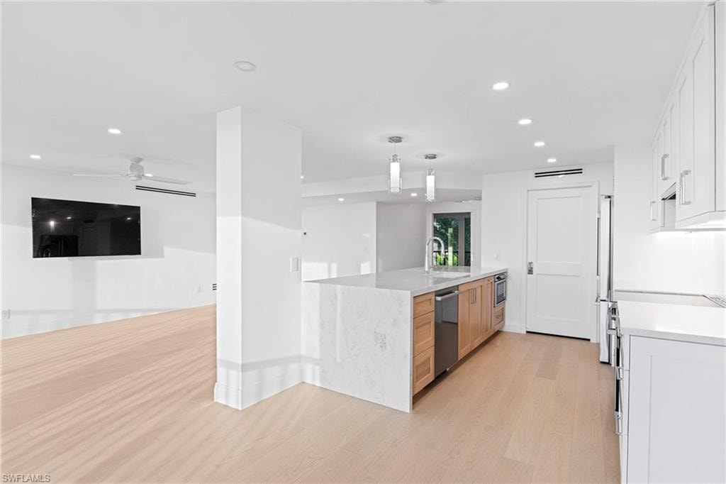 Kitchen with white cabinets, light stone countertops, hanging light fixtures, light wood finished floors, and recessed lighting