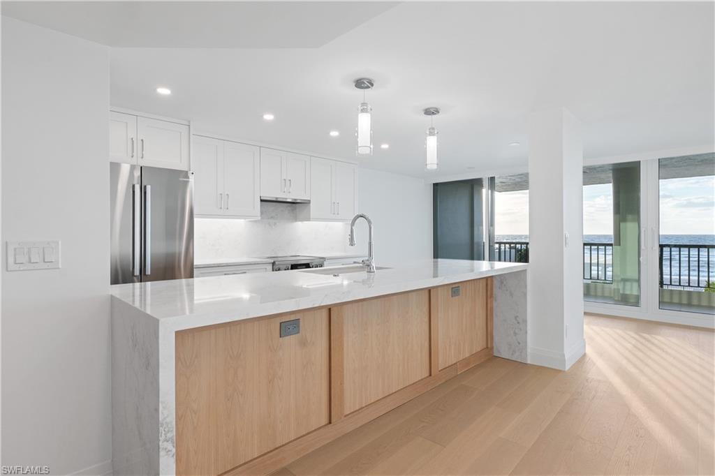 Kitchen with freestanding refrigerator, light stone counters, recessed lighting, white cabinetry, and light wood-type flooring