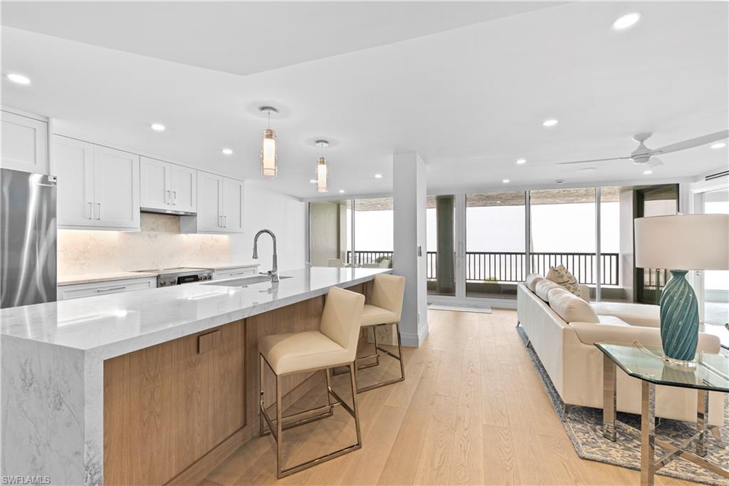 Dual tone kitchen with light stone countertops, light wood finished floors, tasteful backsplash, a kitchen breakfast bar, and two tone cabinetry
