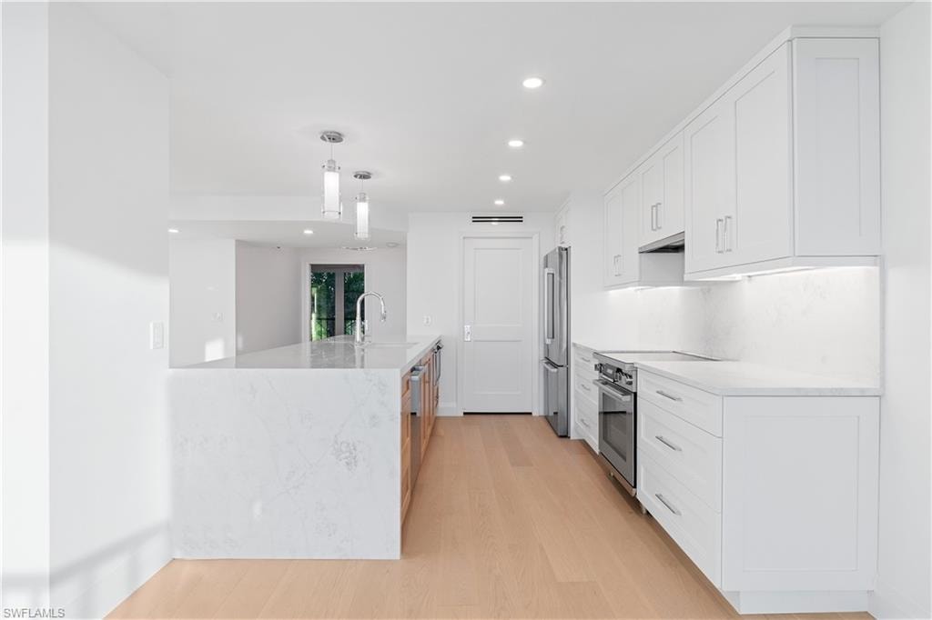 Kitchen featuring white cabinets, recessed lighting, light stone countertops, decorative light fixtures, and stainless steel appliances