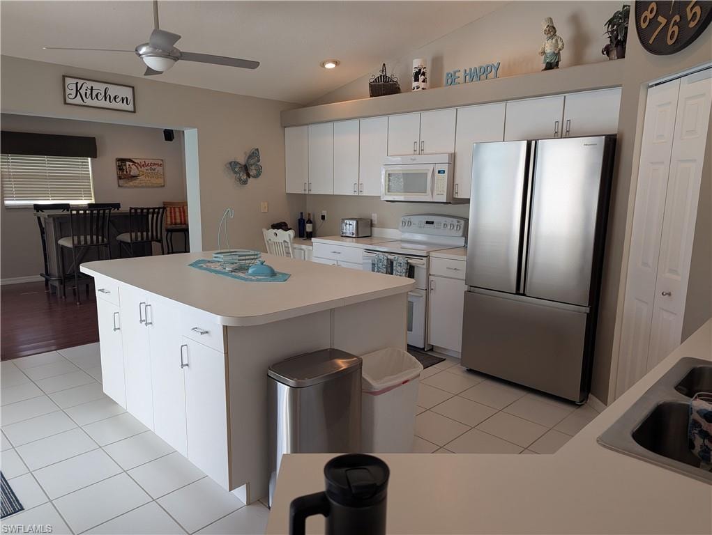 Kitchen with white appliances, white cabinetry, light tile patterned flooring, lofted ceiling, and light countertops