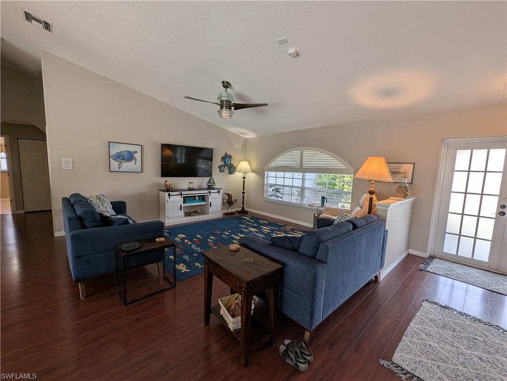 Living area featuring arched walkways, vaulted ceiling, dark wood-type flooring, and a ceiling fan