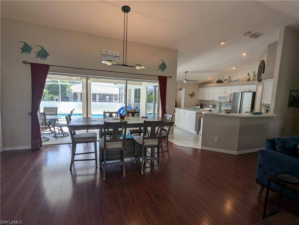 Dining area with dark wood-style floors, vaulted ceiling, and recessed lighting