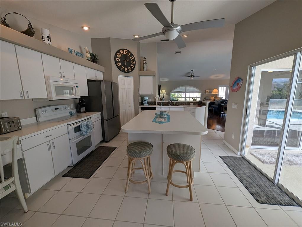 Kitchen featuring a kitchen bar, white appliances, white cabinets, a peninsula, and recessed lighting