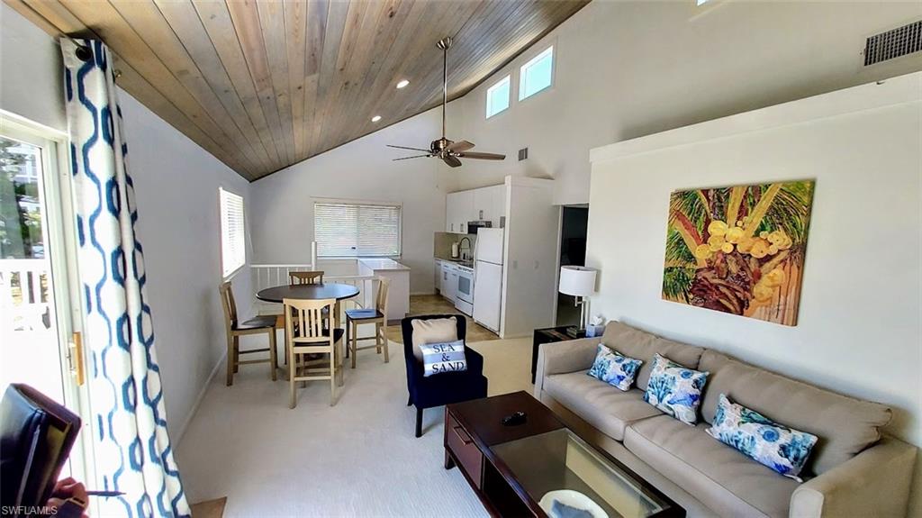 Living room featuring high vaulted ceiling, light colored carpet, a ceiling fan, and wooden ceiling