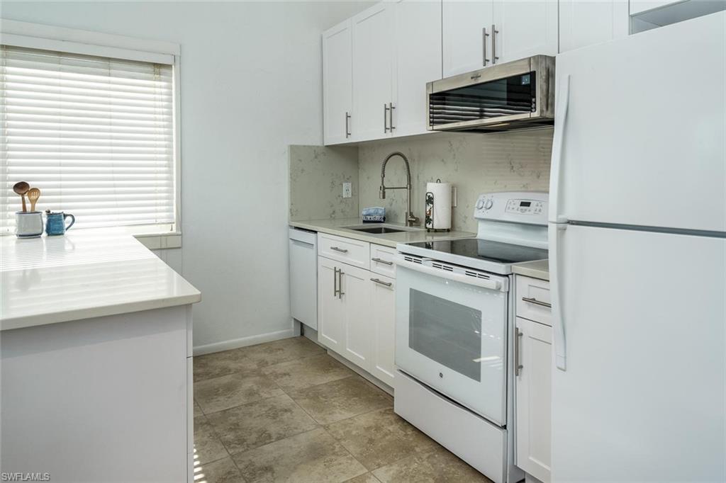 Kitchen with white appliances, white cabinetry, tasteful backsplash, and light stone counters