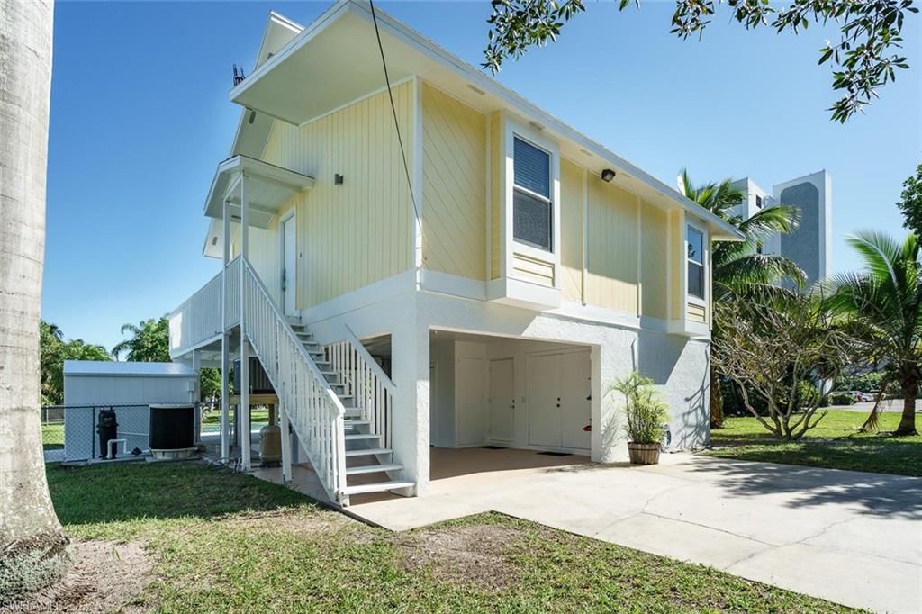Back of house featuring stairs, concrete driveway, a lawn, and a carport