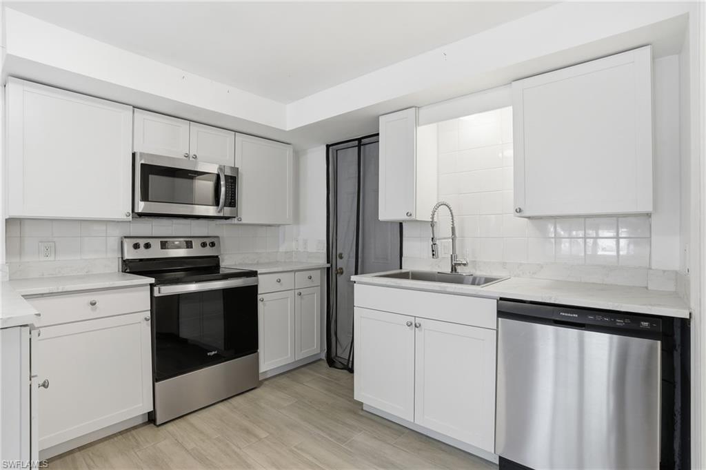 Modern kitchen featuring white shaker cabinetry, stainless steel appliances, light-toned countertops, a white subway tile backsplash, and wood-finish flooring - Virtually Edited Image