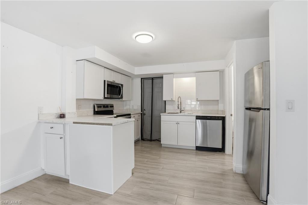 Modern kitchen featuring white cabinetry, light-toned countertops, stainless steel appliances, a white subway tile backsplash, and light wood-finish flooring - Virtually Edited Image