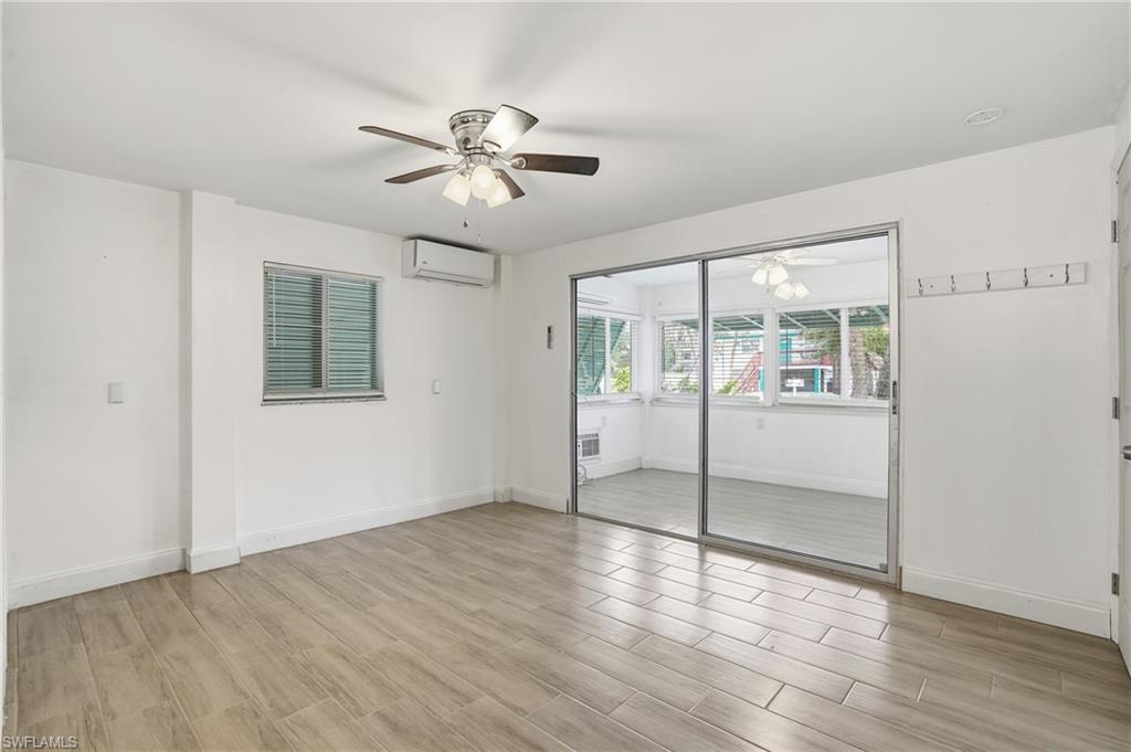 Spacious room featuring wood-finish tile flooring, a ceiling fan with integrated lighting, and a wall-mounted air conditioning unit - Virtually Edited Image