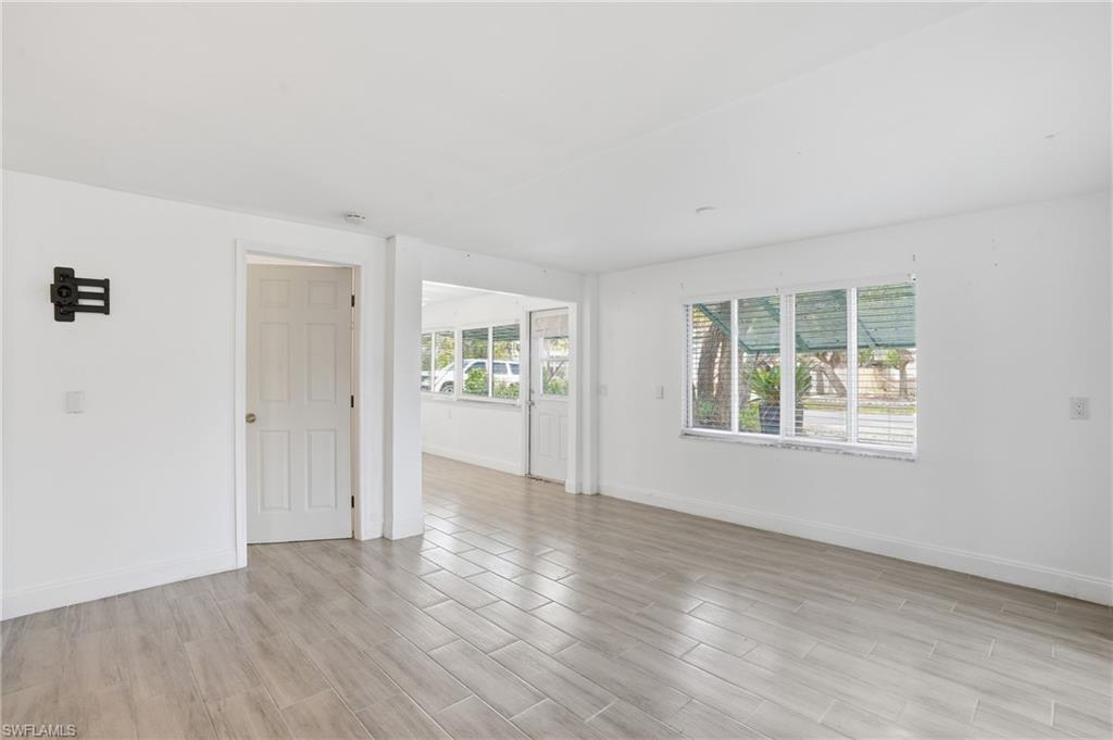 Spacious room featuring light wood-finish flooring, white walls, and a large window with horizontal blinds - Virtually Edited Image