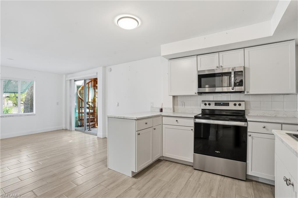 Bright kitchen area featuring white shaker-style cabinetry, light-toned countertops, a stainless steel range, and an over-the-range microwave - Virtually Edited Image