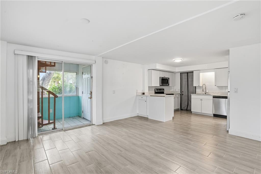 Open-concept living area featuring wood-finish tile flooring and an integrated kitchen - Virtually Edited Image