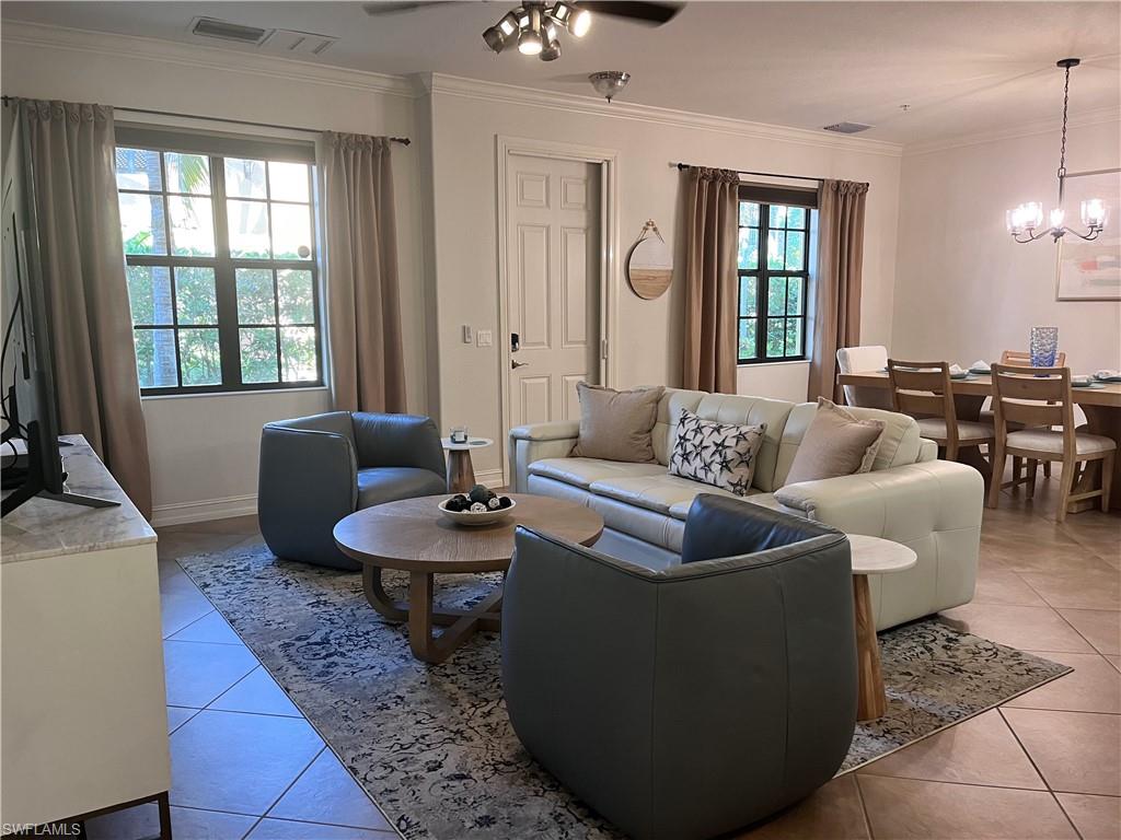 Tiled living room with crown molding, a healthy amount of sunlight, and ceiling fan with notable chandelier