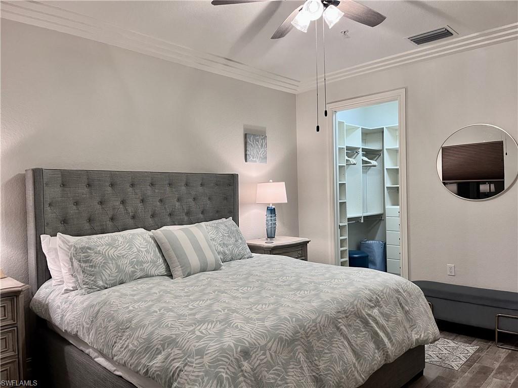 Bedroom with a walk in closet, ornamental molding, ceiling fan, wood-type flooring, and a closet