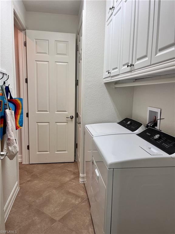 Clothes washing area with cabinets, light tile tiled floors, and washer and dryer