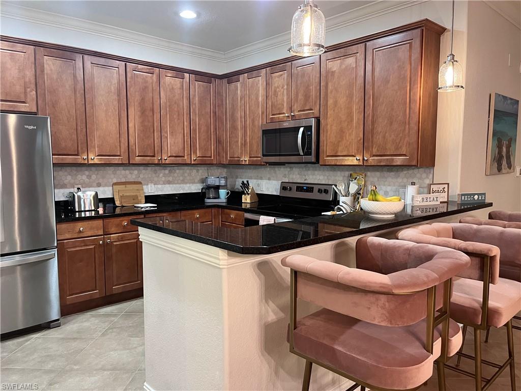 Kitchen with a kitchen breakfast bar, kitchen peninsula, hanging light fixtures, and appliances with stainless steel finishes