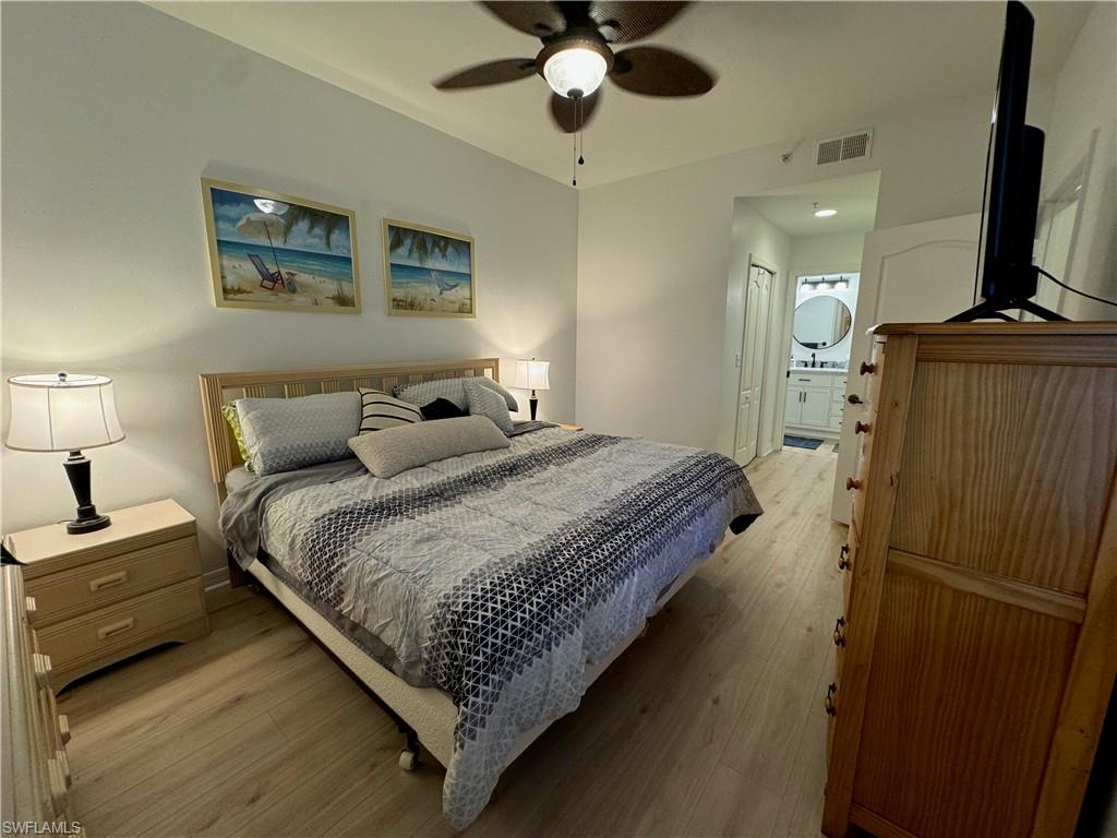 Bedroom with ensuite bath, light hardwood / wood-style floors, ceiling fan, and a closet