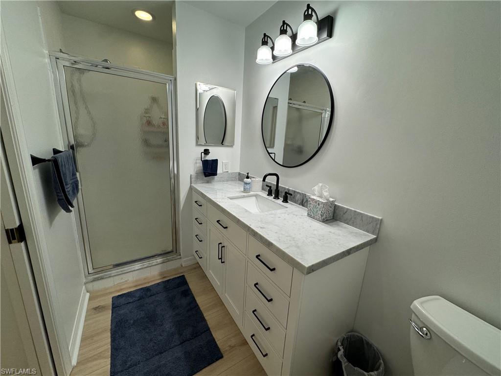Bathroom featuring vanity, hardwood / wood-style flooring, toilet, and a shower with door