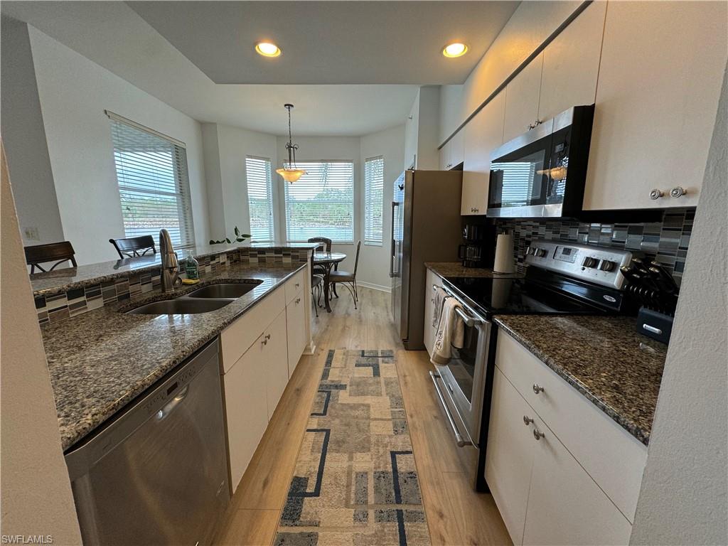 Kitchen featuring stainless steel appliances, a healthy amount of sunlight, decorative light fixtures, and white cabinetry