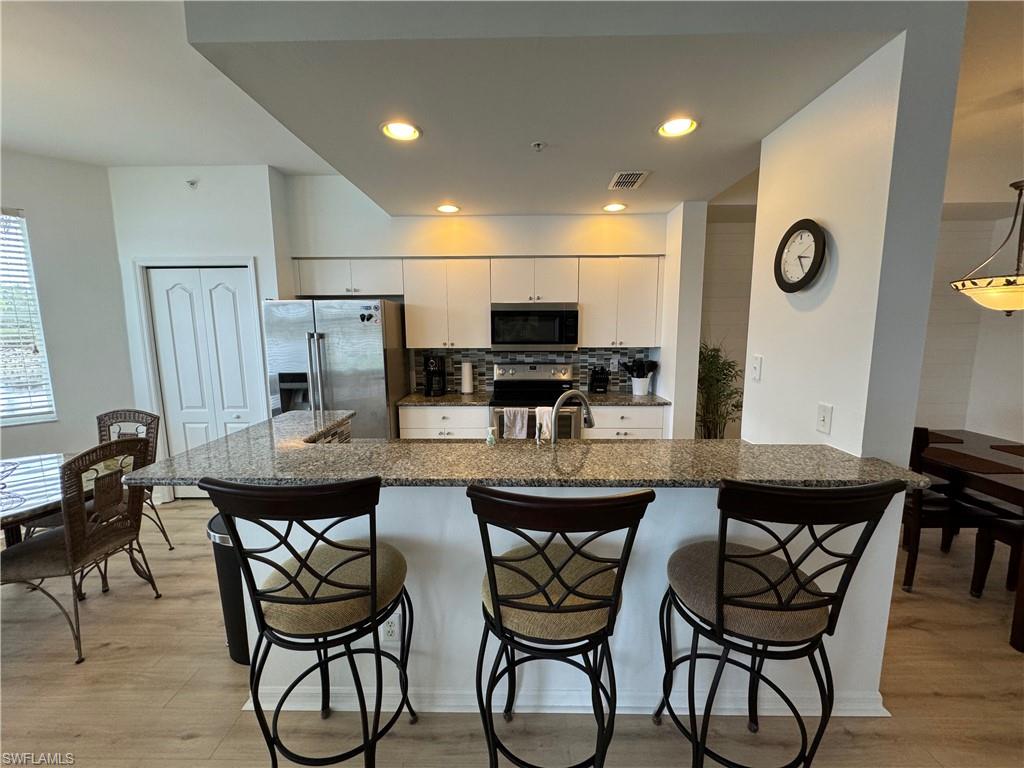 Kitchen with white cabinets, a kitchen breakfast bar, stainless steel appliances, and light hardwood / wood-style floors