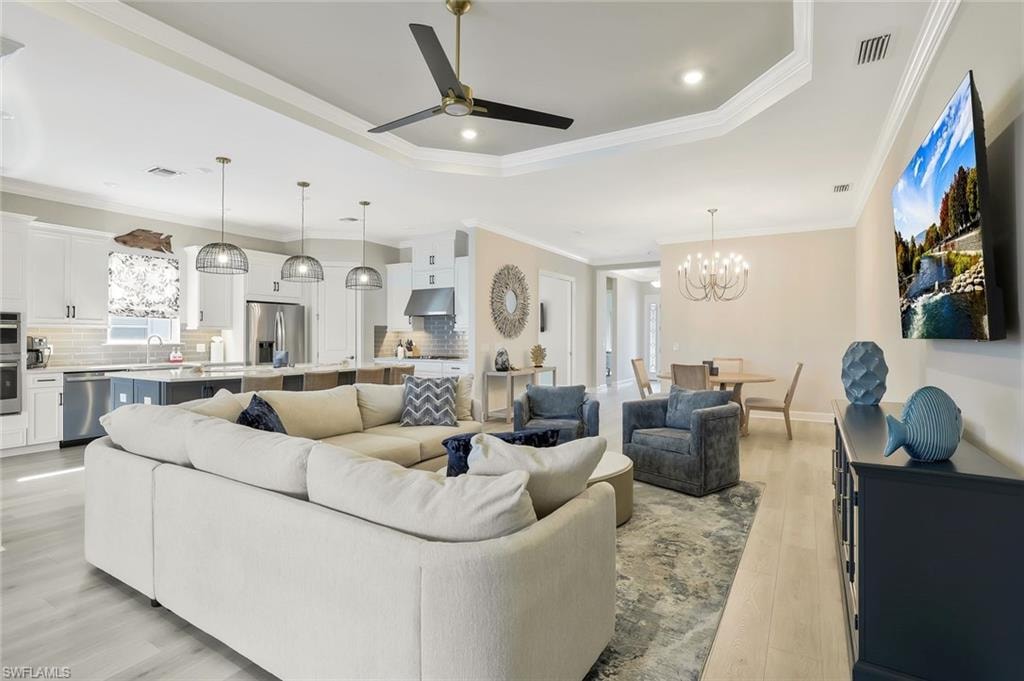 Living room featuring ceiling fan, crown molding, a chandelier, light wood finished floors, and recessed lighting