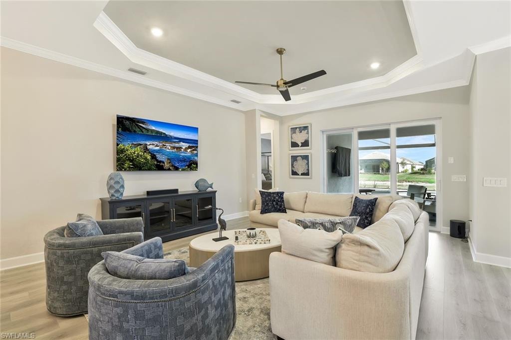 Living room featuring wood finished floors, ornamental molding, ceiling fan, recessed lighting, and a raised ceiling