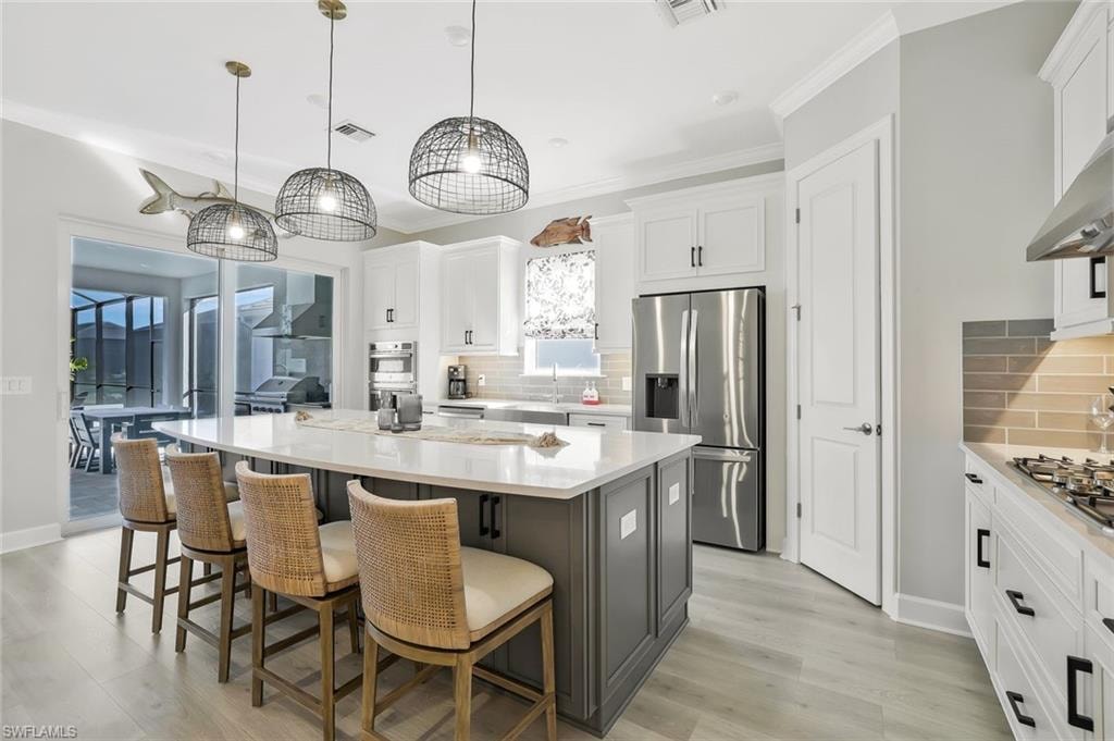 Kitchen with a breakfast bar area, appliances with stainless steel finishes, white cabinets, pendant lighting, and a kitchen island