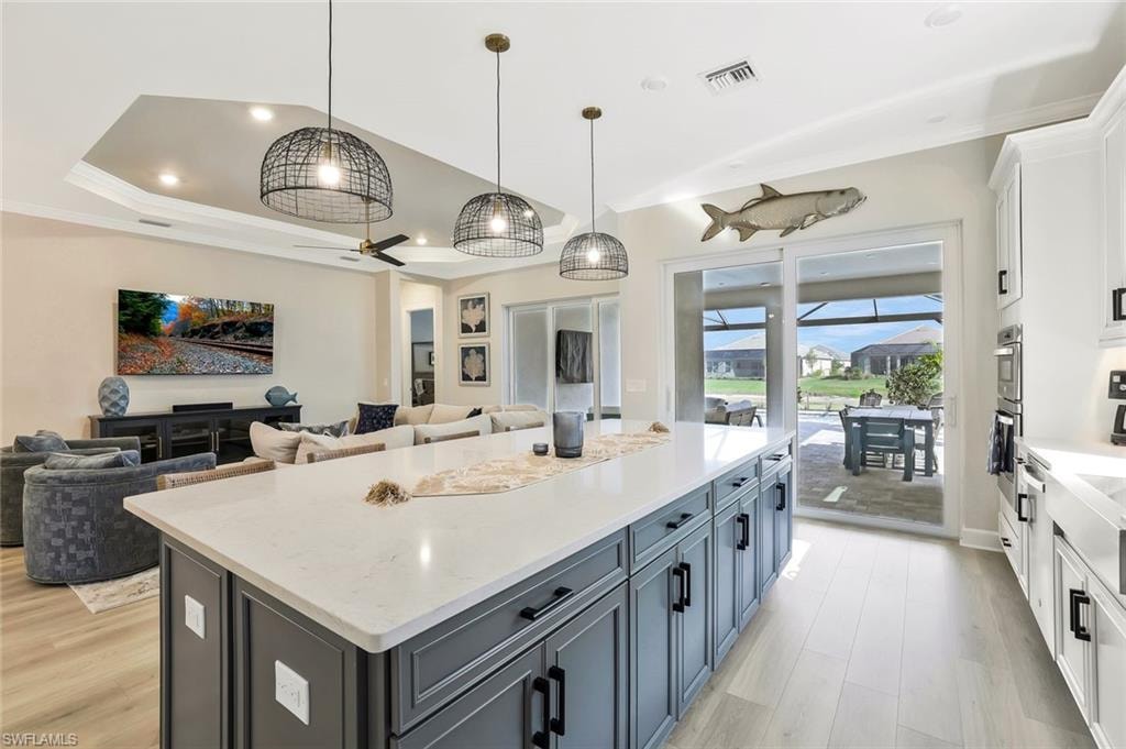 Kitchen with white cabinets, pendant lighting, open floor plan, light stone countertops, and ornamental molding