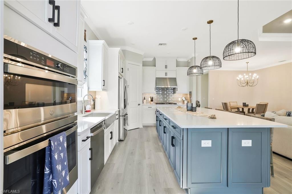 Kitchen with stainless steel appliances, white cabinets, blue cabinets, light wood-style floors, and ornamental molding