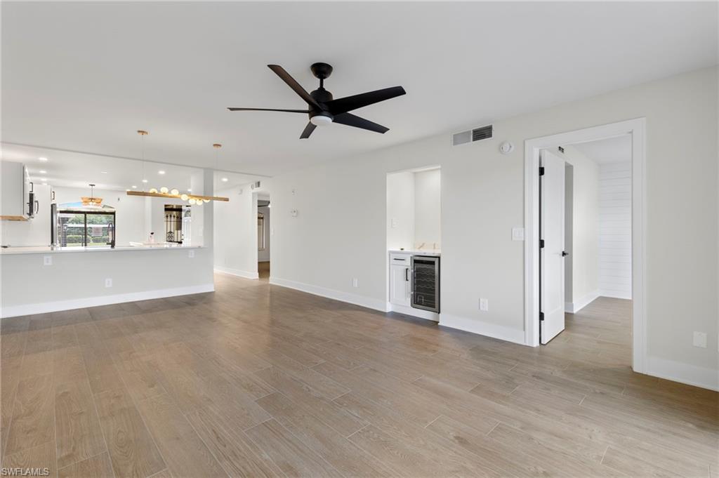 Unfurnished living room with wine cooler, light wood-style floors, ceiling fan, and a chandelier