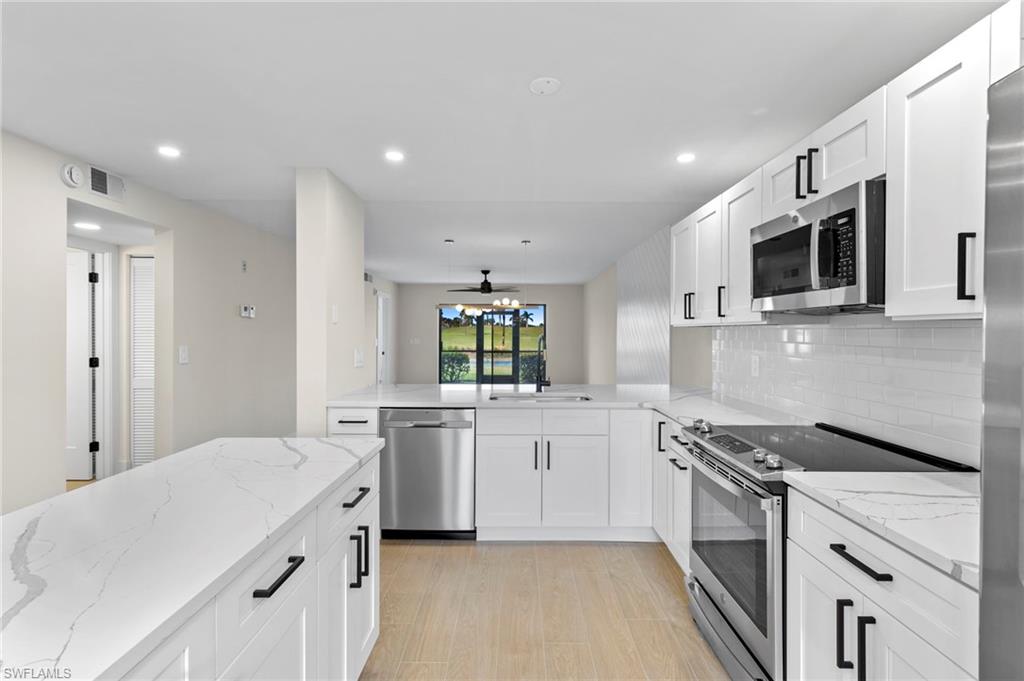 Kitchen with stainless steel appliances, white cabinetry, light stone countertops, a ceiling fan, and recessed lighting