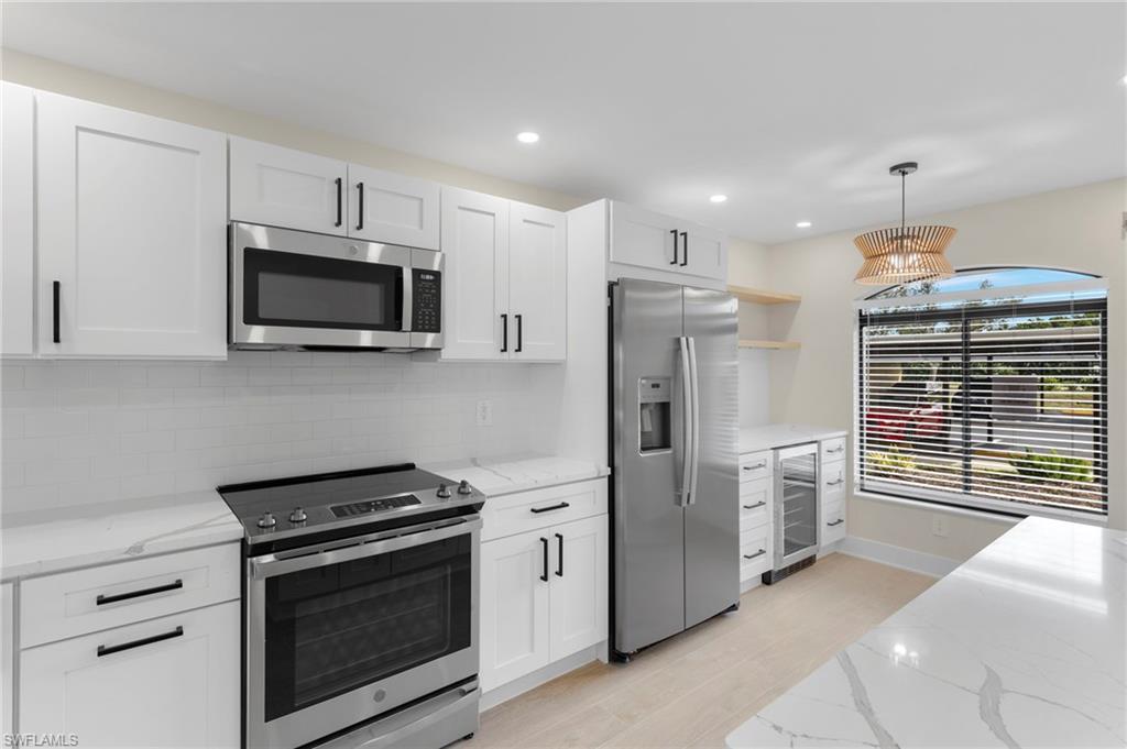 Kitchen with appliances with stainless steel finishes, open shelves, light stone countertops, decorative light fixtures, and white cabinetry