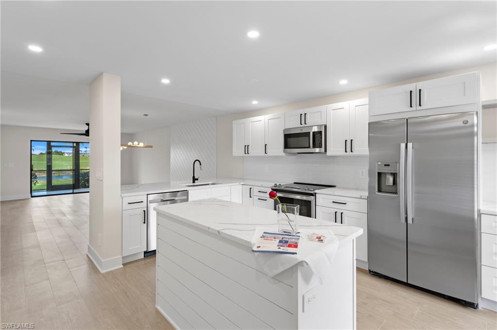 Kitchen with appliances with stainless steel finishes, a peninsula, light stone counters, decorative backsplash, and a kitchen island