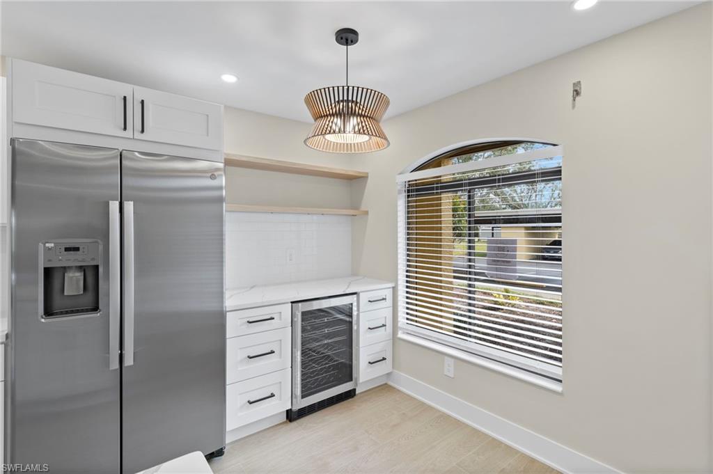 Bar with stainless steel refrigerator with ice dispenser, open shelves, light stone countertops, wine cooler, and backsplash